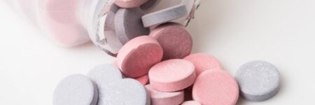 Heartburn pill bottle spilling blue and pink antacid pills on white background; Concept of “Can I take Pepcid or Prilosec Indefinitely?”