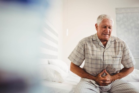 An elderly man in the bedroom is clutching his stomach, experiencing the pain of colon cancer