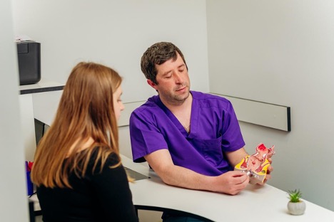 During a hospital consultation, a proctologist shows an artificial rectum model to a female patient, explaining how to treat hemorrhoids